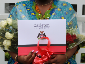 A graduate holds their Carleton University degree and white roses at Convocation