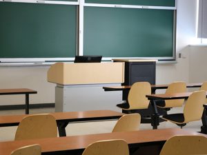 A shot of desks and attached chairs in front of a speaking podium and chalkboards, in a Tory Building classroom.