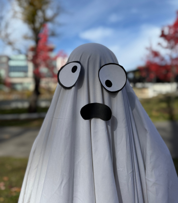 A person dressed as a ghost wearing a white sheet with paper googly eyes and mouth.
