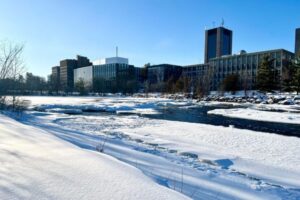 Campus buildings seen across the Rideau River, which is covered in a blanket of snow.