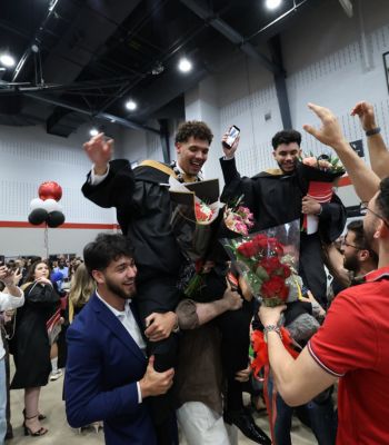 Two graduating students cheering and being lifted up by their family and friends at Convocation.