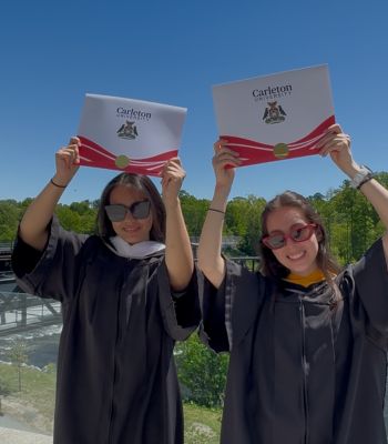 Two students holding up their Carleton University diplomas on a sunny day. 