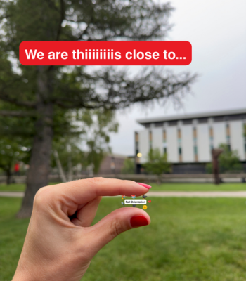 A hand holding a small text which says "Fall Orientation" with a larger text that says "We are this close to..." and the Quad as the background.