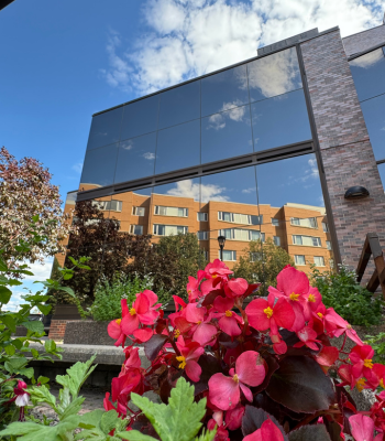 The Prescott House reflected in Minto Centre's windows, with red and pink flowers in the front.